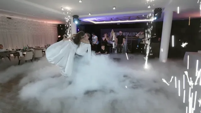 Mladenci plešu u niskom dimu dok iza njih pršte prskalice, a bend svira na pozornici