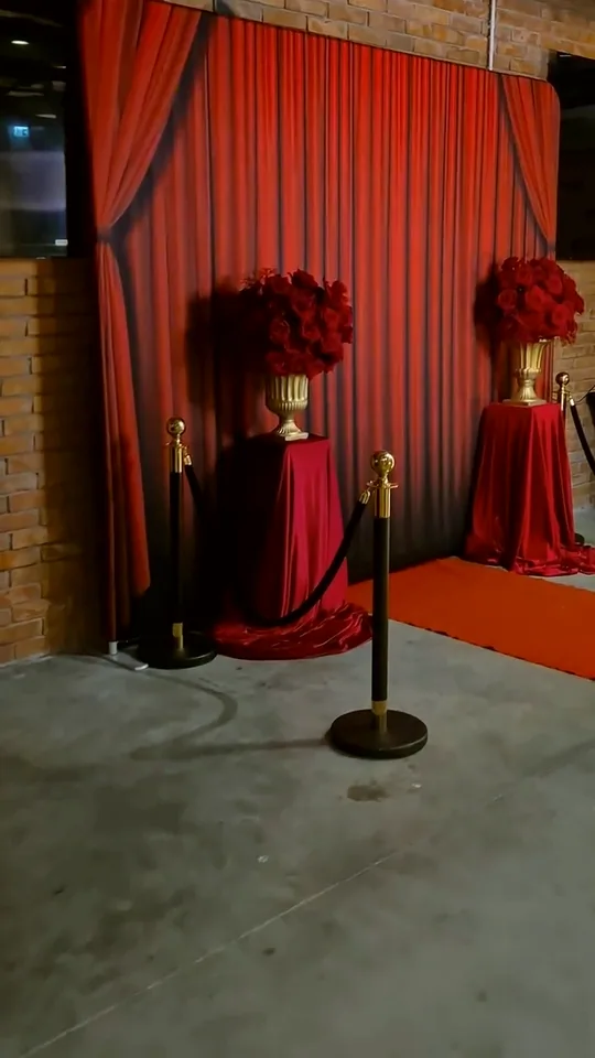 Photobooth kutak s crvenim zastorom, crvenim ružama u zlatnim vazama i crvenim tepihom