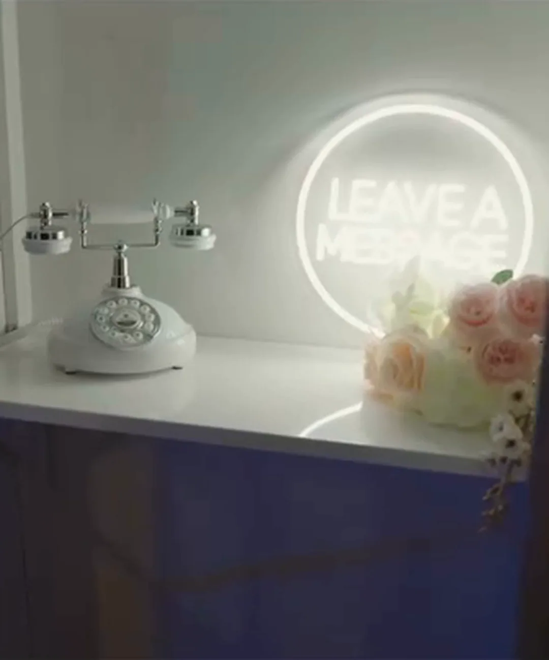 Bijeli starinski telefon za glasovne poruke gostiju ispod svjetlećeg natpisa Leave a message