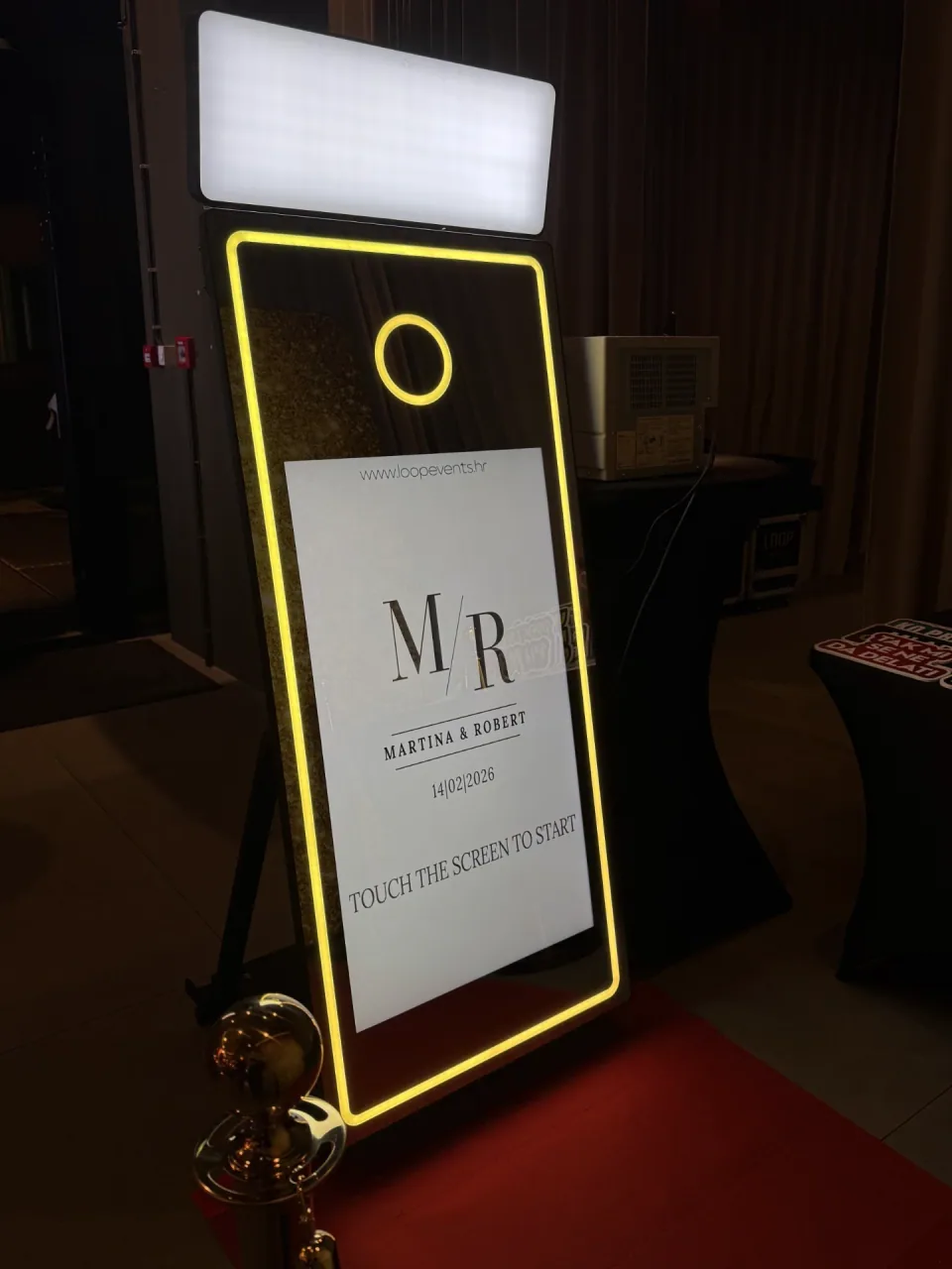 Mirror photobooth sa zlatnim svjetlećim rubom i personaliziranim ekranom dobrodošlice s inicijalima mladenaca